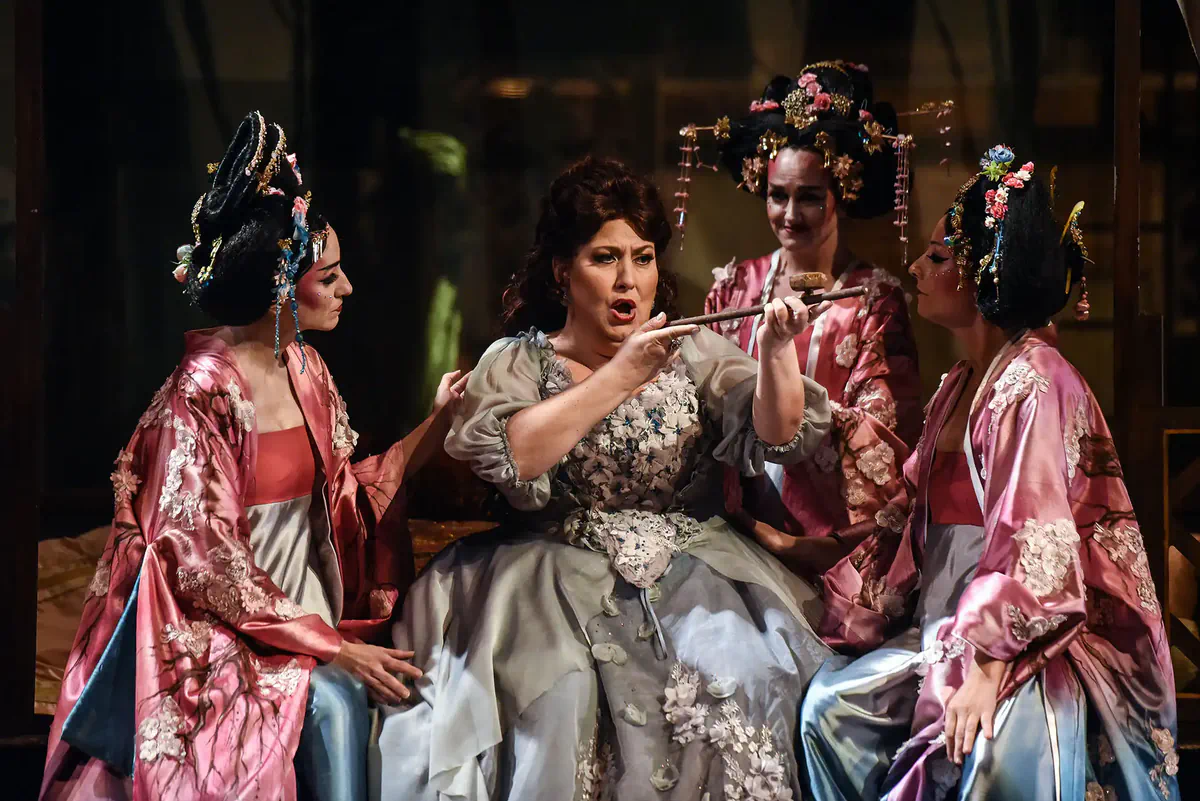 Escena de Un ballo in maschera con una cantante en el centro rodeada por tres intérpretes vestidas con trajes inspirados en la estética japonesa.